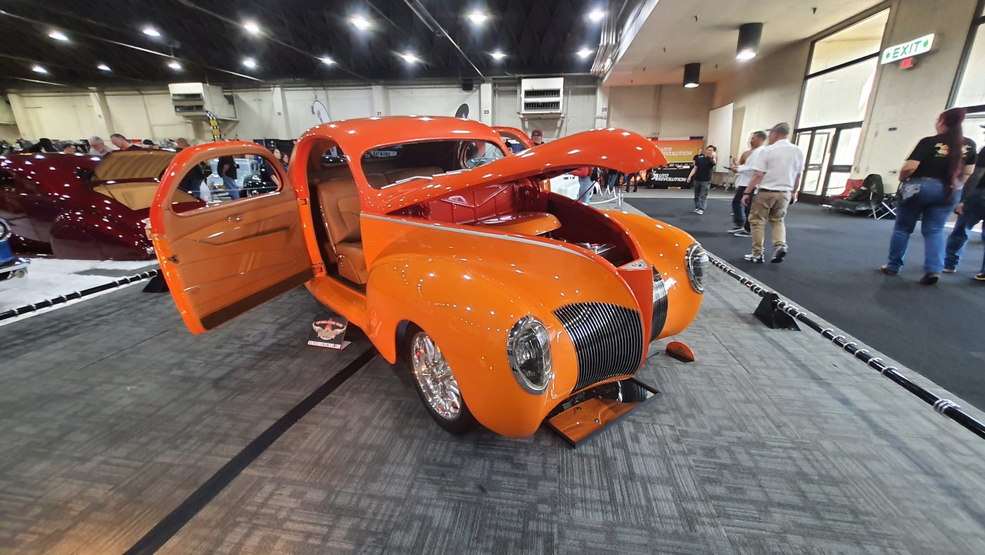 Pomarańczowy Ford Deluxe coupe 1940 z otwartymi drzwiami i maską